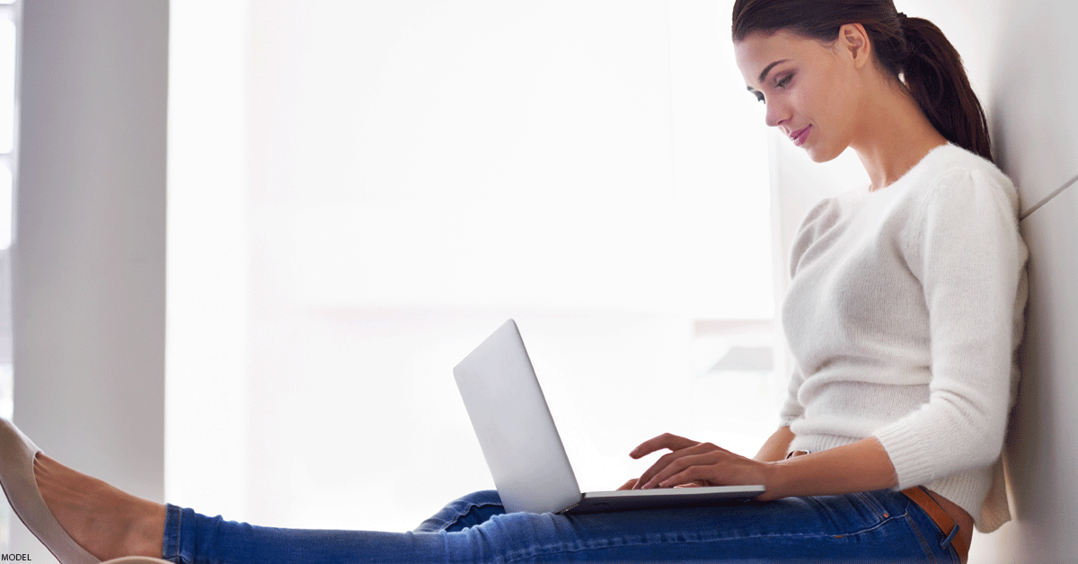 Woman sitting with back against wall browsing on laptop computer