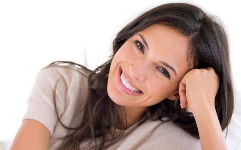 Woman with smooth skin smiling at camera leaning head against one hand