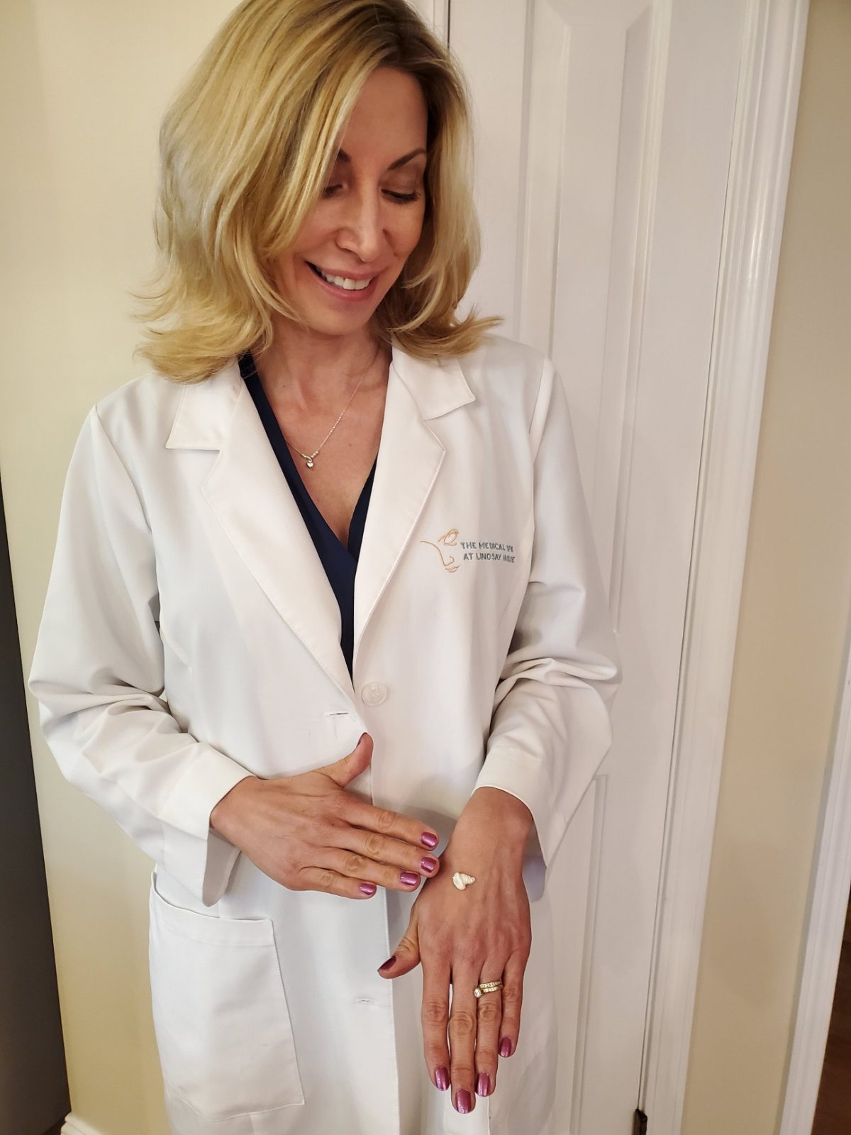 Woman in lab coat applying Revision Lumiquin anti-aging lotion to hand