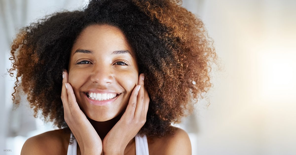 Woman with face in hands smiling at camera