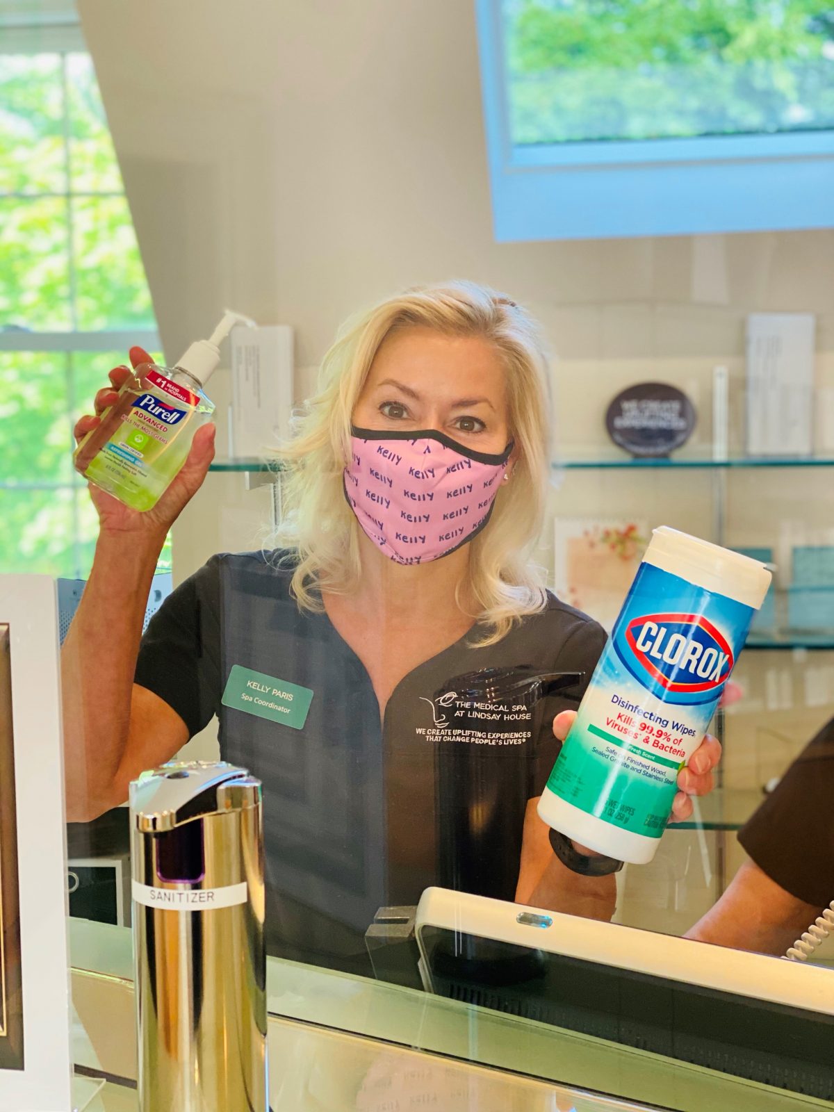 Licensed cosmetologist Kelly W. wearing mask and holding disinfectant cleaners